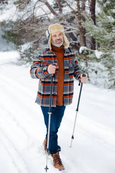 Morning activity. Contented man with scandinavian sticks in a snowy forest