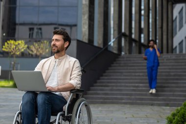 Dizüstü bilgisayarı olan. Hastanenin avlusunda tekerlekli sandalyede otururken dizüstü bilgisayarda çalışan engelli serbest çalışan bir adam.
