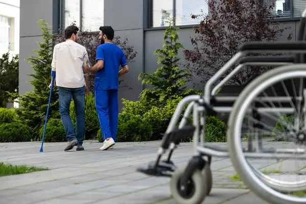 Rehabilitation center. Male nurse having a walk with a patient in a rehabilitation center