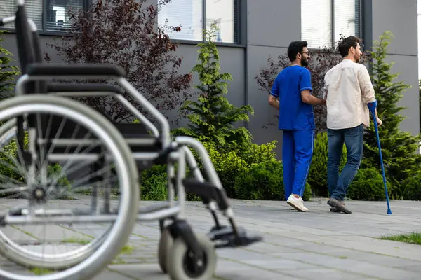 Rehabilitation center. Male nurse having a walk with a patient in a rehabilitation center