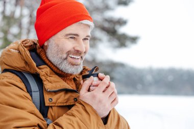 Isınıyor. Karlı bir ormanda elinde termosla bir adam