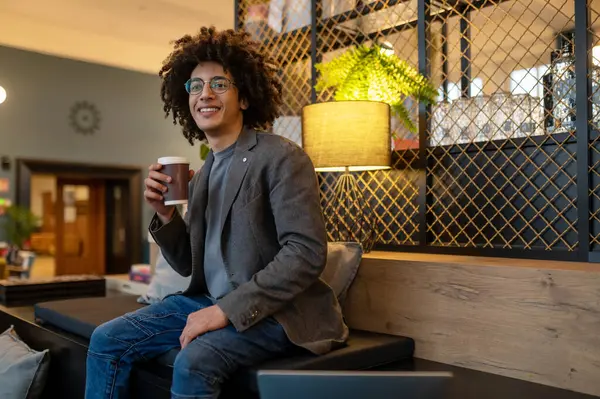 Coffee break. Smiling curly-haired man sitting with coffee cup in hands