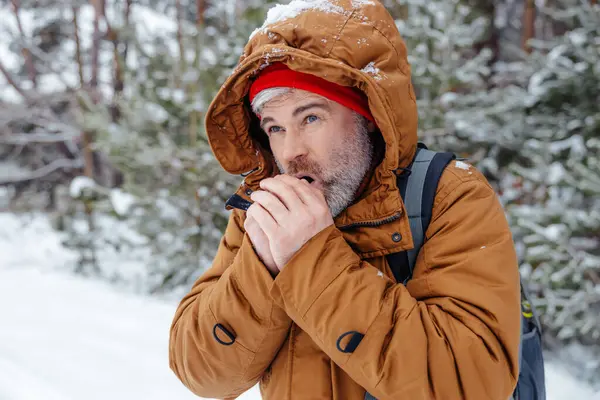Cold weather. Man in warm jacket getting cold in a winter forest