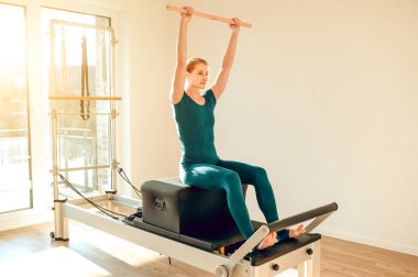Spordaki atletik kadın yoga stüdyosundaki reformist makinede zarif bir şekilde pilates yapıyor.