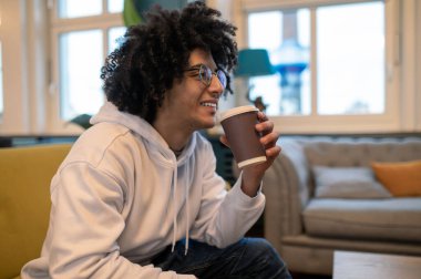Kahve zamanı. Kıvırcık saçlı genç adam kahve içiyor ve rahatlamış görünüyor.