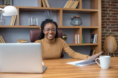 Rasta bukleli çekici bir kadın ev içi ofis içi bilgisayar ve teknoloji kullanarak online iş yapıyor.