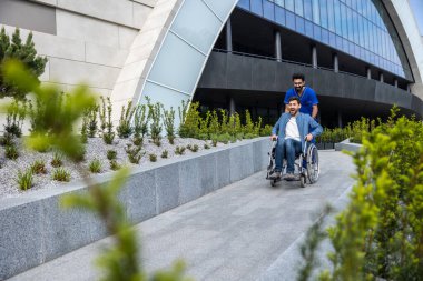 Engelli. Erkek hemşireyle yürürken tekerlekli sandalyede oturan yakışıklı adam.