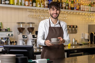 Kahvehanenin yanında elinde bir fincan kahve tutan gülümseyen bir barmen.