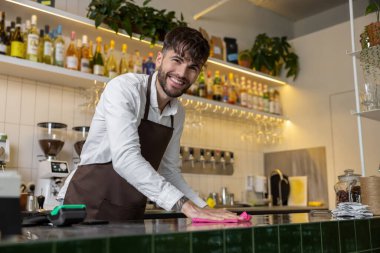 Sakallı erkek barmen. Kafede tezgahı siliyor.