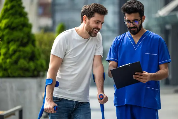 Rehabilitation Man Crutches Male Nurse Blue Uniform Walking Hospital Yard — Stock Photo, Image