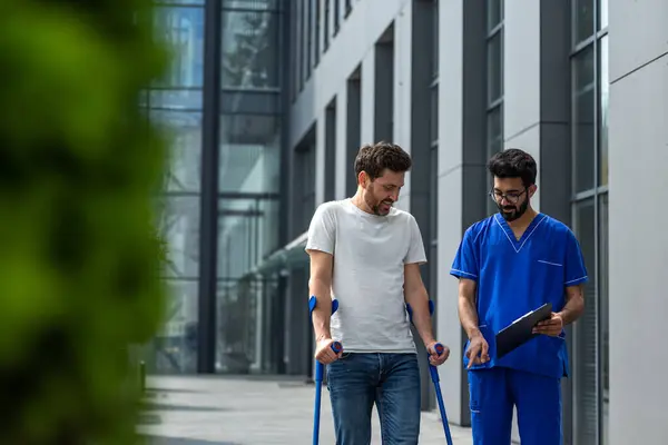 Rehabilitation Man Crutches Male Nurse Blue Uniform Walking Hospital Yard — Stock Photo, Image