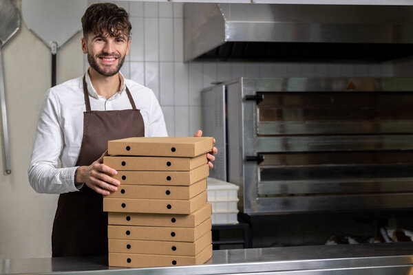 Man cafe worker holding cardboard stack of pizza boxes preparing for shipping and delivery