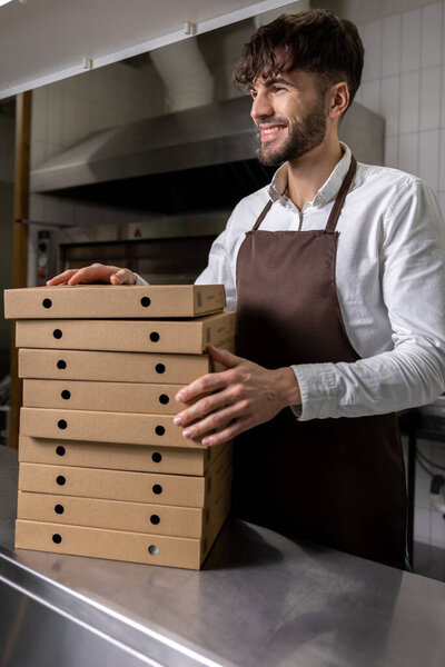 Man cafe worker holding cardboard stack of pizza boxes preparing for shipping and delivery