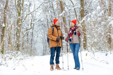 Aktif insanlar. Olgun bir çift İskandinav sopalarıyla karlı bir ormanda yürüyüş yapıyor.