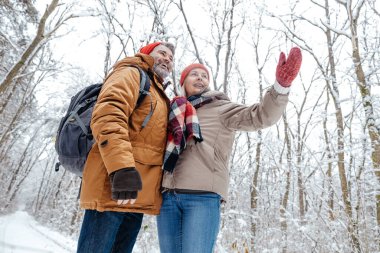 Winter. Mature couple in a snowy forest feeling excited clipart
