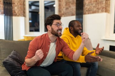 İki arkadaş birlikte televizyon seyredip heyecanlı görünüyor.