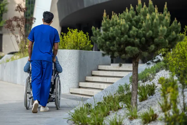 Walk Patient Male Nurse Blue Doctors Overall Carrying Wheelchair — Stock Photo, Image