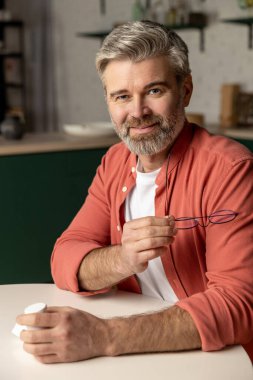 Evde oturan turuncu tişörtlü çekici adam.