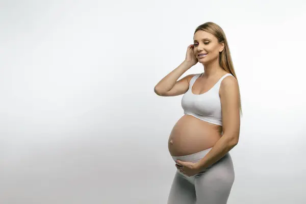 怀孕的女人穿着白衣的金发孕妇看上去很体贴 — 图库照片