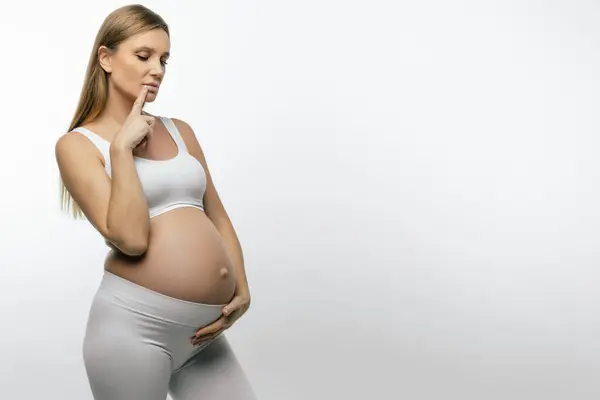 怀孕的女人穿着白衣的金发孕妇看上去很体贴 — 图库照片