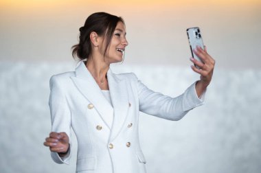 Video message. Woman in white jacket recording a video message and looking excited clipart