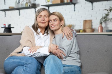 Güzel bir son sınıf öğrencisi ve yetişkin kızı evdeki kanepede otururken sarılıp gülümsüyorlar.