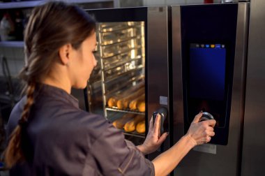 Fırıncı kadın fırında Fransız ekmeği pişirmek için elektrikli fırın kullanıyor.