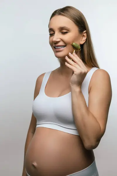 面部按摩可爱的怀孕年轻女子用滚筒按摩她的脸 — 图库照片