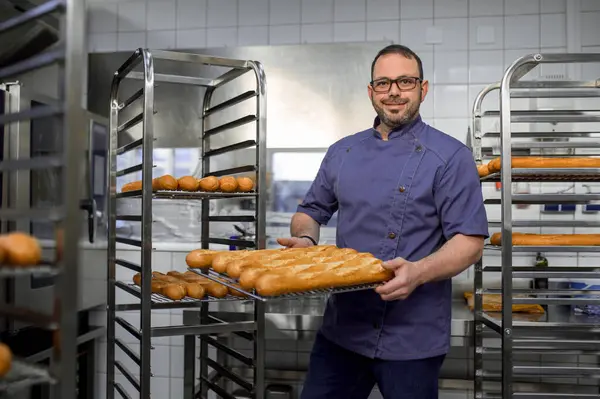 Tukang Roti Berseragam Memegang Baguette Atas Nampan Dengan Rak Roti — Stok Foto