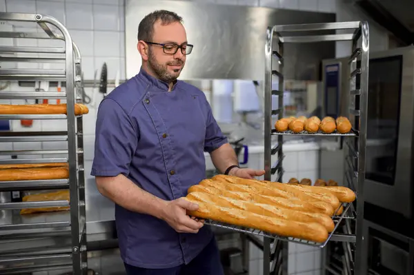 Tukang Roti Berseragam Memegang Baguette Atas Nampan Dengan Rak Roti — Stok Foto