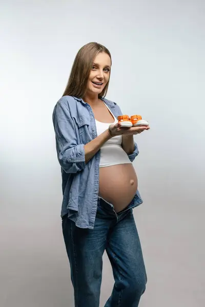 我在等孩子大肚皮的孕妇穿着橙色可爱的婴儿鞋 图库图片