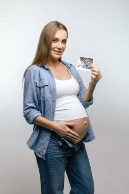 Röntgen sonucu. Uzun saçlı hamile kadın röntgen sonuçlarını gösteriyor ve gülümsüyor.