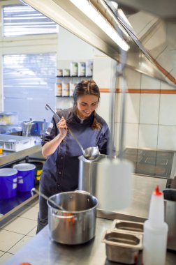 Çorba pişiriyorum. Genç bir kadın mutfakta çorba pişiriyor ve elinde bir kepçeyle