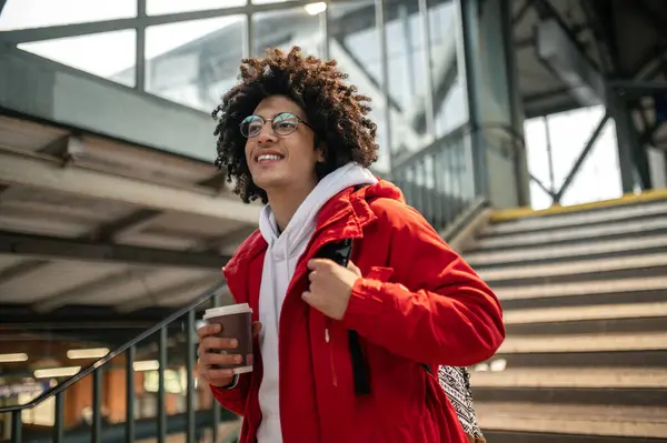 Young guy at the railway station. Curly-haired young guy holding a coffee cup and looking excited