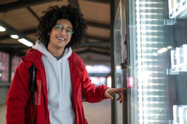 Tren istasyonunda. Kıvırcık saçlı genç adam trenin zaman çizelgesini inceliyor.