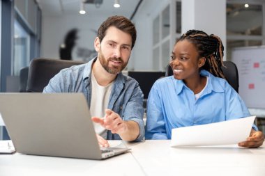 Modern ofiste oturan çok kültürlü meslektaşlar yeni iş projeleri yaratmak için dizüstü bilgisayar kullanıyorlar.