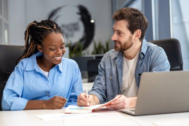 Modern ofiste oturan çok kültürlü meslektaşlar yeni iş projeleri yaratmak için dizüstü bilgisayar kullanıyorlar.