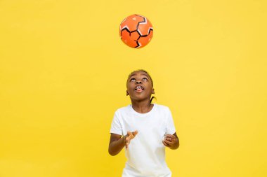 Spor giyim sektöründe, sarı arka planda izole edilmiş futbol topuyla oynayan çok kültürlü bir çocuk.