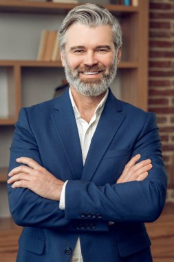 Arkadaş canlısı orta yaşlı psikoterapist adam resmi kıyafetler giyiyor ve ofiste gülümsüyor.