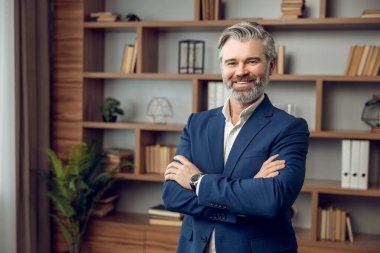 Kendine güvenen sakallı, modern ofiste poz veren şık takım elbiseli bir psikoterapist.