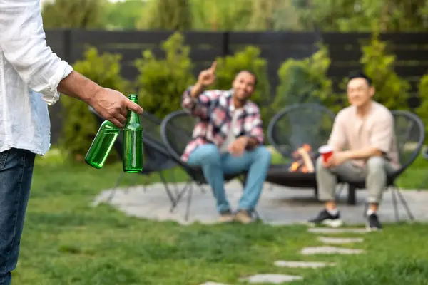 Friendly men meeting friend with cold beer during backyard party