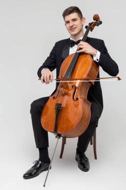 Sandalyede oturan müzisyen beyaz arka planda izole edilmiş çello çalıyor.