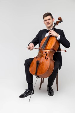 Smokin giyen erkek sanatçı, açık gri arka planda izole edilmiş kaçak eşya çalıyor.