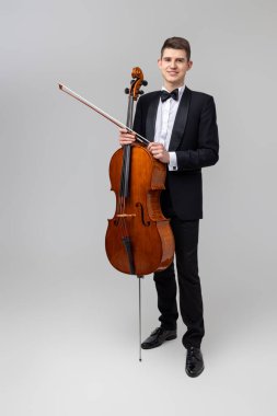 Smokin giyen erkek sanatçı, açık gri arka planda izole edilmiş kaçak eşya çalıyor.