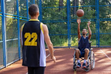 Tekerlekli sandalyedeki basketbolcu dışarıda arkadaşlarıyla maç yapıyor.