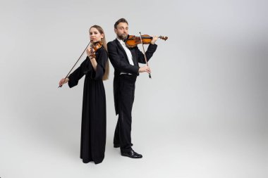 Sakallı adam ve genç kadın kemancı konserde klasik müzik çalıyorlar açık gri arka planda izole edilmiş.