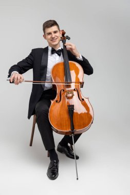 Tutkulu çellocu, beyaz arka planda izole edilmiş bir şekilde koltukta oturmuş konser veriyor.