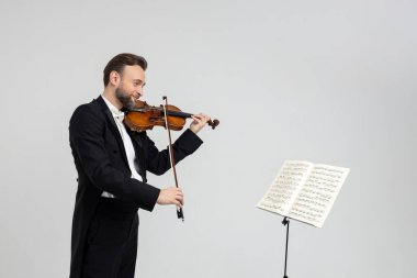 Kemancı sakallı erkek keman çalıyor, notaların önünde keman çalıyor, beyaz arka planda tek başına duruyor.