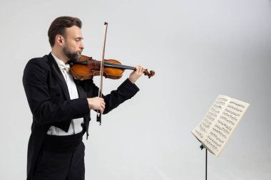 Kemancı sakallı adam keman çalarken beyaz arka planda izole edilmiş müzik notalarıyla yüzleşiyor.