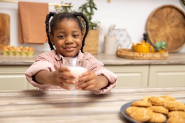 Sevimli küçük siyah kız mutfakta atıştırmalık süt ve kurabiye yiyor.